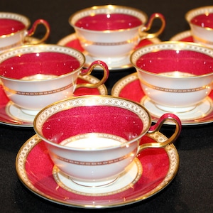 May include: A set of six teacups and saucers. The cups and saucers are white with a red interior and rim. Gold trim accents the edges and handles. The saucers are red with a white center and gold trim. A classic tea set.