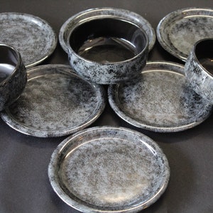 May include: Set of six black and grey speckled ceramic bowls and plates. The bowls and plates have a mottled, textured surface.