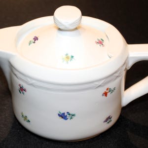 May include: White porcelain teapot with a lid and a handle. The teapot is decorated with small, colorful flowers.