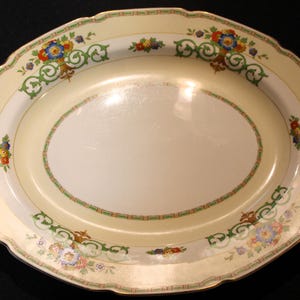May include: A large oval serving platter with a cream-colored background and a green, gold, and floral design. The platter has a scalloped edge and a gold rim.