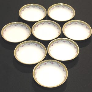 May include: A set of seven white porcelain dishes with a floral design and gold trim. The dishes have a scalloped edge with a delicate pink and green floral pattern around the rim. The gold trim adds a touch of elegance to the overall design.