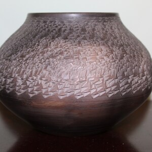 May include: A dark brown ceramic vase with a textured surface. The vase has a round body and a wide opening.