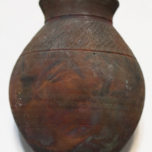 May include: A brown ceramic vase with a rounded body and a slightly flared opening. The vase has a textured surface and a dark brown glaze with hints of red and green.