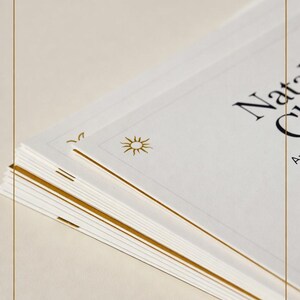 May include: A stack of white paper with gold accents and text. The text reads "Natal Chart". The paper is framed with a gold border and zodiac symbols. The sun symbol is also visible.