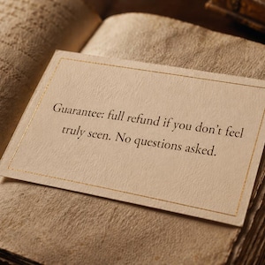 May include: An open book with aged, textured pages. A cream-coloured card with gold trim rests on the pages, displaying the text: "Guarantee: full refund if you don't feel truly seen. No questions asked."