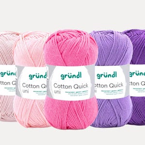 Op de afbeelding: Vijf bollen katoenen garen in verschillende roze en paarse tinten. Elke bol heeft een label met "Cotton Quick uni" van "gründl". Het garen is strak opgerold, ideaal voor brei- of haakprojecten.