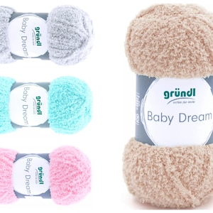 Könnte beinhalten: Vier Knäuel Garn in verschiedenen Farben: Grau, Hellblau, Rosa und Beige. Das Garn ist weich und flauschig, und das Etikett lautet "gründl Baby Dream".