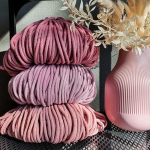 May include: Three spools of pink and purple cotton rope, stacked on top of each other. The rope is thick and textured, and the colors are soft and muted.
