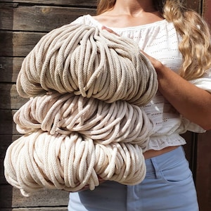 Puede incluir: Un montón grande de cuerda de algodón beige natural, sostenido por las manos de una persona. La cuerda es gruesa y texturizada, perfecta para manualidades.