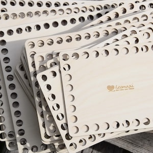 Könnte beinhalten: Ein Stapel quadratischer Holzrahmen mit runden Löchern zum Weben. Der oberste Rahmen trägt den Text "leomaxi" und ein Herz mit einer Stricknadel.