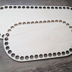 Könnte beinhalten: Zwei unfertige Holz-Korb-Böden. Die Böden sind oval geformt und haben gleichmäßig verteilte Löcher am Umfang zum Weben. Das Holz hat eine helle, natürliche Farbe und sichtbare Maserung. Die Böden sind zum Basteln bereit.