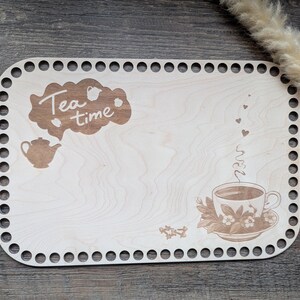 Può includere: Un vassoio di legno chiaro con un bordo decorativo di fori distanziati uniformemente. Il vassoio presenta immagini incise di una teiera, una tazza da tè e le parole "Tea time" in un design a forma di nuvola. La tazza da tè ha vapore con cuori.