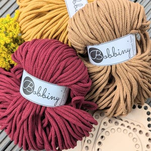 May include: Three balls of cotton rope in mustard yellow, tan, and burgundy. The rope is labelled "Bobbiny Premium 5mm Cotton Cord".