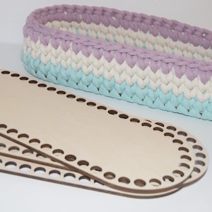 May include: Three oval-shaped wooden loom boards with holes around the edges. A crocheted basket with a light blue, white and purple striped pattern sits on top of the loom boards.