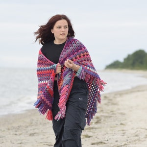 Könnte beinhalten: Eine Frau trägt einen bunten Häkel-Schal mit Fransen am Strand.