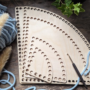 Könnte beinhalten: Eine Sammlung von vier unfertigen Holz-Korbunterteilen in verschiedenen Größen, jeweils mit gleichmäßig verteilten Löchern am gebogenen Rand. Ein Häkelhaken und eine hellblaue Kordel sind ebenfalls vorhanden. Die Artikel sind auf einer Holzoberfläche angeordnet.