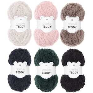 Könnte beinhalten: Sechs Knäuel Garn in verschiedenen Farben, darunter Beige, Rosa, Braun, Dunkelblau und Grün. Jedes Knäuel hat ein weißes Etikett mit dem aufgedruckten Text "creative TEDDY".