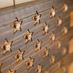 May include: A wooden American flag with bullet casings used as stars. The flag is made of dark wood with a light wood grain pattern.
