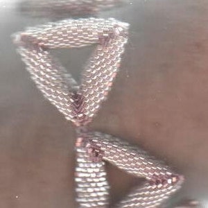 May include: Two silver-toned triangular shapes, made of small beads, are stacked on top of each other. The shapes are connected at the points, creating a three-dimensional design.