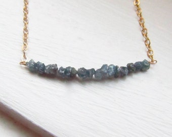 May include: A delicate gold chain necklace with a row of small, rough, gray-blue gemstones.