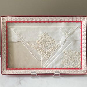 May include: A set of three white handkerchiefs with delicate lace trim, packaged in a red box with a decorative border.