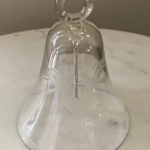 May include: A clear glass bell with a silver chain and an etched design of a dove with outstretched wings.