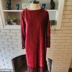 May include: A long, red velvet dress with black embroidered details on the sleeves and hem. The dress has a round neckline and long sleeves.