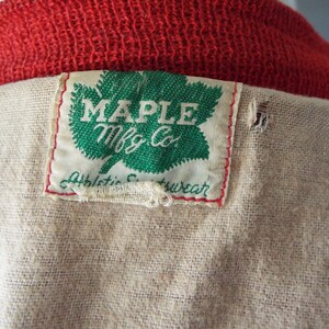 May include: A white tag with green maple leaf and the text "MAPLE Mfg Co." and "Athletic  Wear" sewn onto a beige fabric.