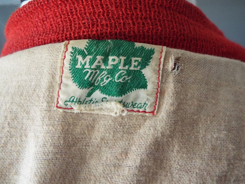 May include: A white tag with green maple leaf and the text "MAPLE Mfg Co." and "Athletic  Wear" sewn onto a beige fabric.