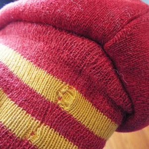 May include: Red and gold striped knit cuff of a sweater. The cuff has two gold stripes.