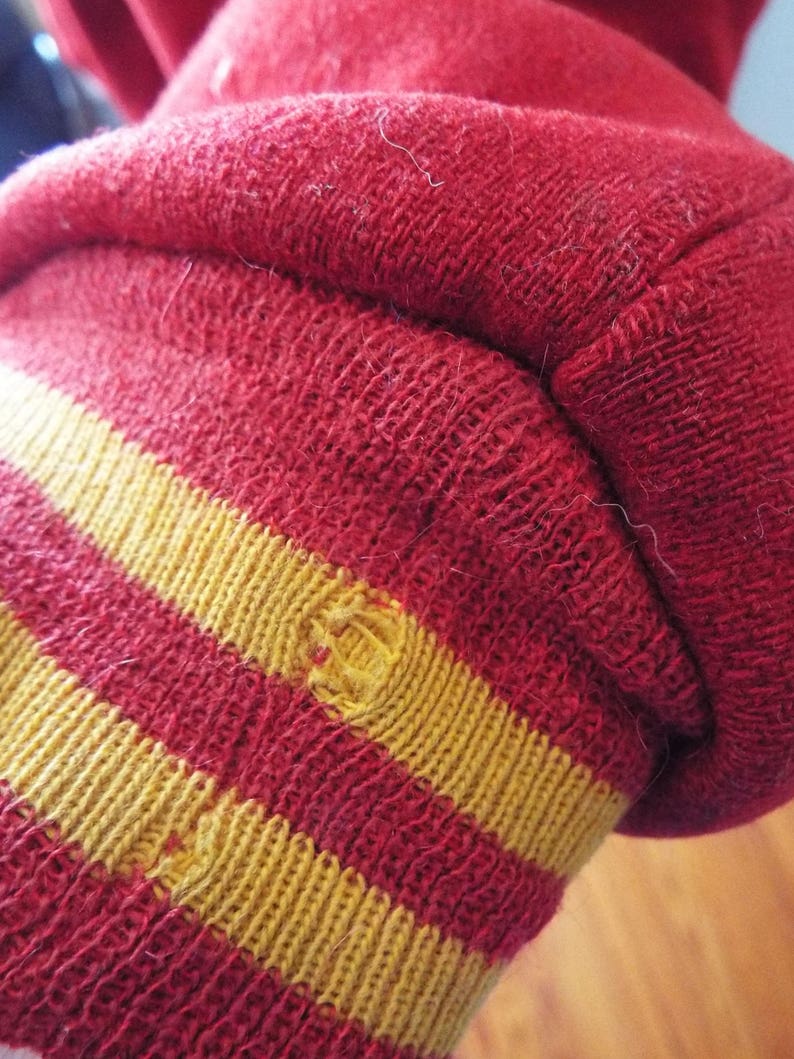 May include: Red and gold striped knit cuff of a sweater. The cuff has two gold stripes.