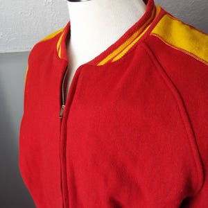 May include: Red wool varsity jacket with yellow and white striped trim around the collar and sleeves.