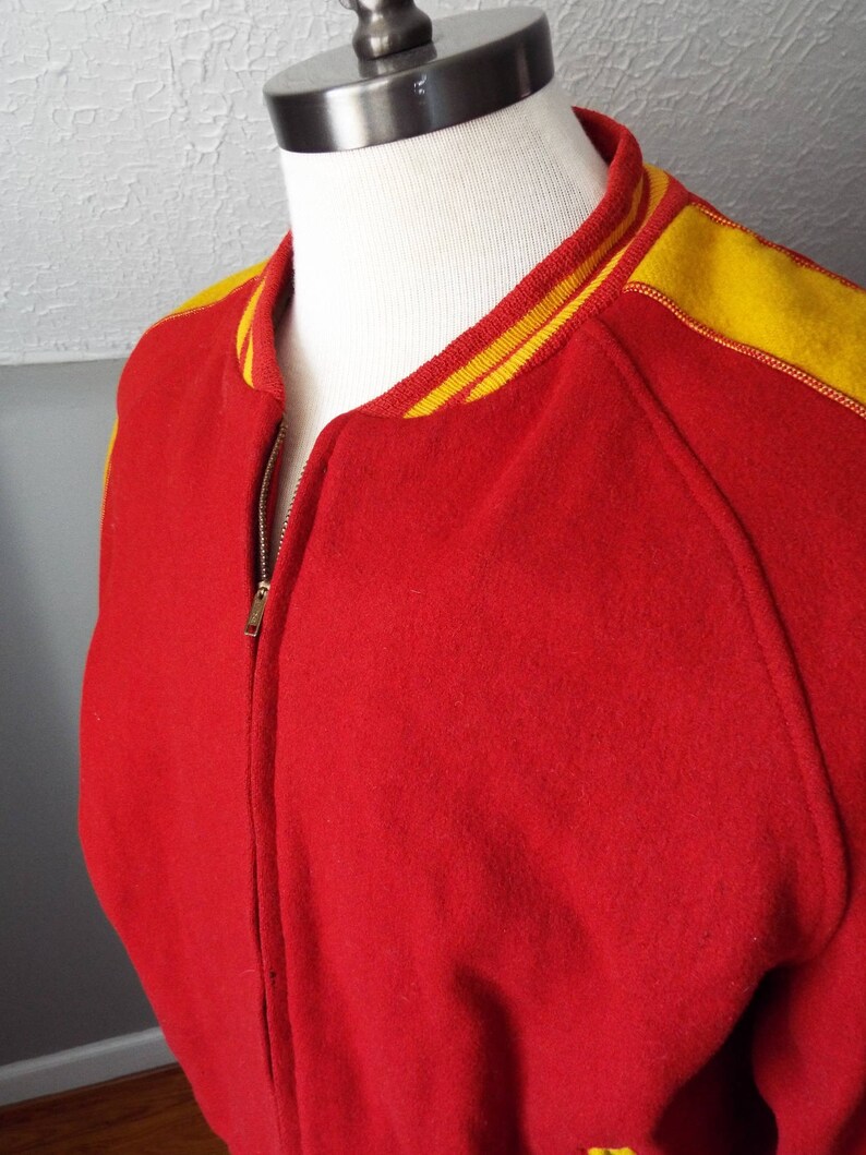 May include: Red wool varsity jacket with yellow and white striped trim around the collar and sleeves.