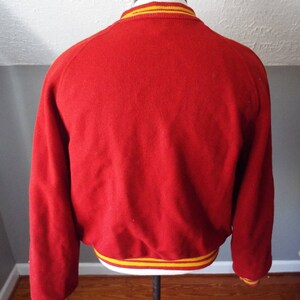 May include: Red wool varsity jacket with yellow and white striped trim around the collar, cuffs, and hem.