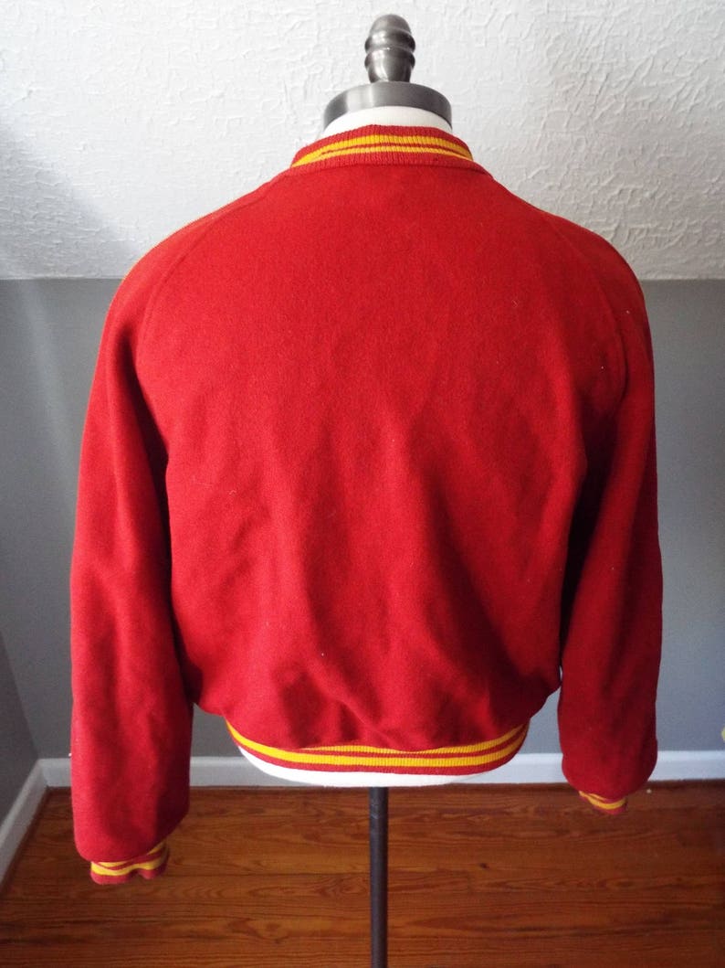 May include: Red wool varsity jacket with yellow and white striped trim around the collar, cuffs, and hem.