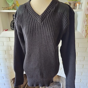 Może przedstawiać: Czarny sweter z dzianiny o prążkowanym splocie, z dekoltem w kształcie litery V i naszywką na każdym ramieniu.