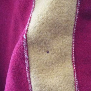 May include: Close-up of a red and yellow fabric with a white stitched seam. The fabric has a fuzzy texture.