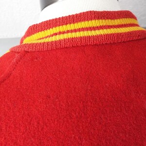 May include: Red varsity jacket with yellow and red striped collar and cuffs.