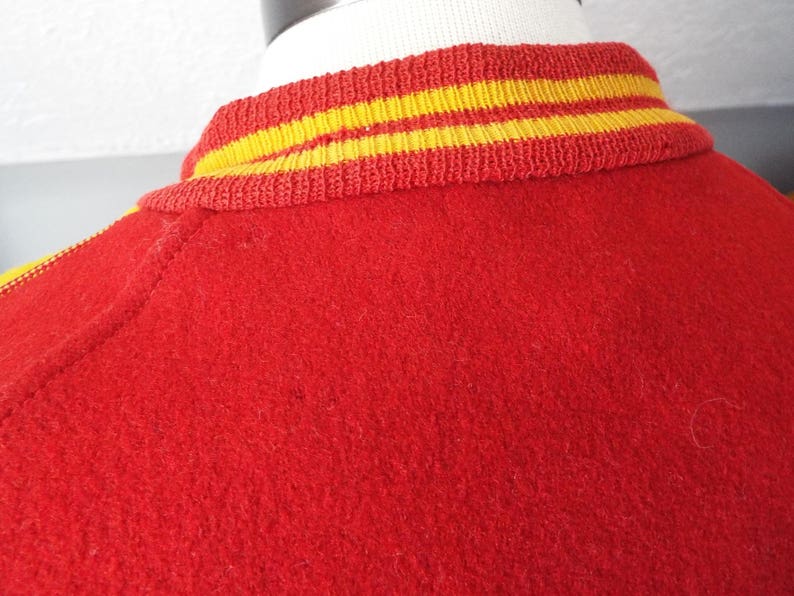 May include: Red varsity jacket with yellow and red striped collar and cuffs.