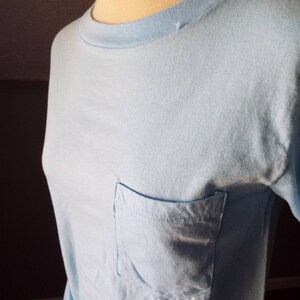 May include: A light blue t-shirt with a single pocket on the left side.