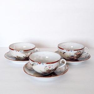 May include: Three white porcelain teacups and saucers with a floral and bird design. The cups and saucers have a gold rim.