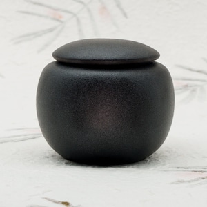 Peut inclure: Un pot en céramique noire avec un couvercle. Le pot a une finition lisse et mate.