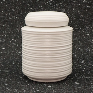 Puede incluir: Jarrón de cerámica blanco con diseño de nervaduras. El jarrón tiene tapa y es perfecto para guardar objetos pequeños.