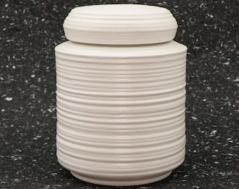 May include: White ceramic jar with a ribbed design. The jar has a lid and is perfect for storing small items.