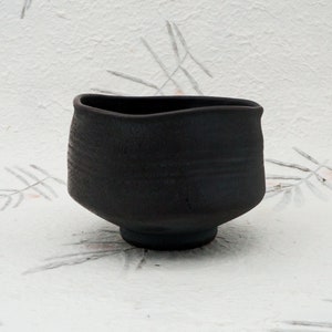 May include: A black ceramic teacup with a slightly uneven rim and a textured surface.