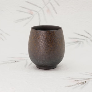 May include: A dark brown ceramic cup with a textured surface. The cup is round and has a wide base.
