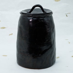 Könnte beinhalten: Eine schwarze Keramikdose mit Deckel und Henkel. Die Dose hat eine glatte, glänzende Oberfläche.