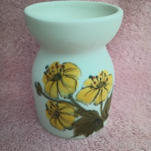 May include: A white ceramic vase with a flared top and a bulbous base. The vase is decorated with yellow floral designs and brown leaves. The vase is approximately 5 inches tall.