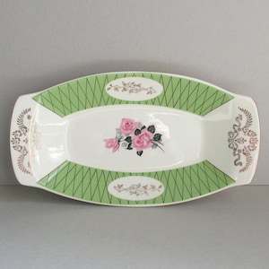 May include: A white oval serving dish with a green and gold geometric design. The centre of the dish features a pink rose floral pattern.