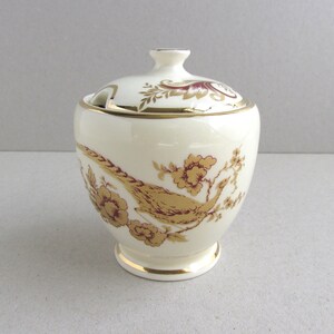 May include: A white ceramic sugar bowl with a lid, decorated with a gold and red pheasant design. The bowl has a gold trim around the rim and base.